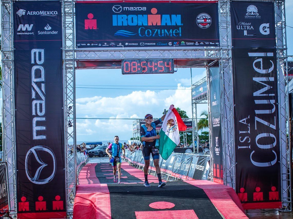 Adriana Carreño cruzando la meta de IRONMAN Cozumel con la bandera de México
